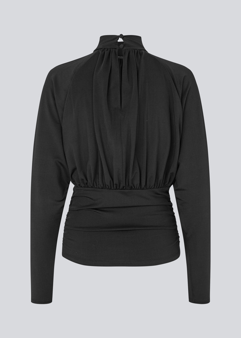 Elegant black blouse featuring a high neckline and long sleeves. Designed with delicate gathered details at the bust and waist to create a flattering silhouette. A subtle button closure at the back of the neck adds a refined and feminine touch. The stretchy fabric ensures a comfortable fit, while the draped design offers timeless elegance. Perfect for both everyday wear and special occasions.