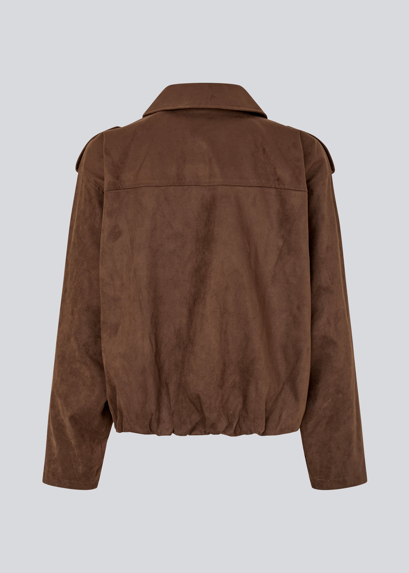 Short brown jacket made from a soft, suede-like material. Features a classic shirt collar, hidden zip and button closure at the front, and practical front pockets. The structured shoulders with strap details and the slightly elasticated hem add a modern, tailored touch. A versatile and stylish piece, perfect for transitional weather and everyday wear.