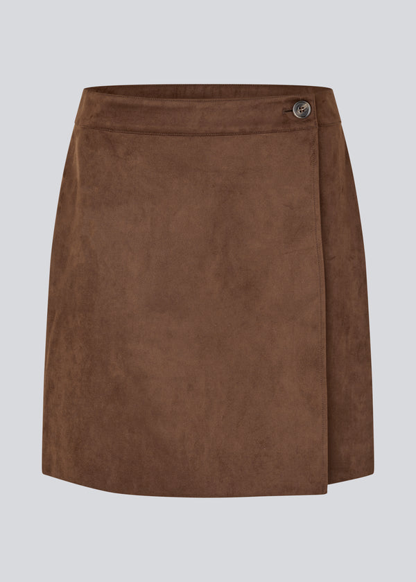Short brown skirt in a suede-look fabric featuring an elegant wrap design. Closes with a decorative side button, adding a sleek and feminine touch. The soft material ensures a comfortable fit, while the minimalist cut makes it easy to style for both casual and more formal occasions. 