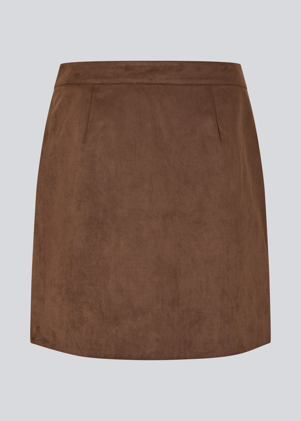 Short brown skirt in a suede-look fabric featuring an elegant wrap design. Closes with a decorative side button, adding a sleek and feminine touch. The soft material ensures a comfortable fit, while the minimalist cut makes it easy to style for both casual and more formal occasions. 