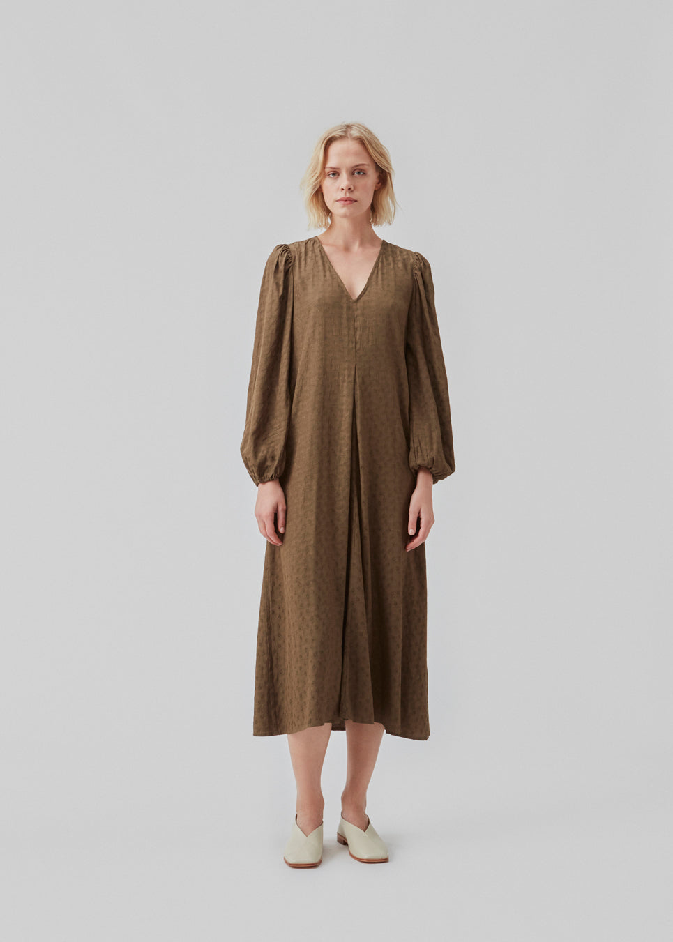 Long dress with long puff sleeves in a shiny satin with a pattern. CarmelMD dress is detailed by a deep v-neck and pleat for extra width in the skirt.  The model is 177 cm and wears a size S/36.