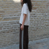 Loose brown trousers with wide legs and a relaxed fit. Featuring an elastic waistband with drawstring for a comfortable, adjustable waist. White side stripes add a sporty and modern touch to the otherwise classic design. Perfect for casual everyday wear or more elevated styling – easy to pair with everything from t-shirts to dressy tops.