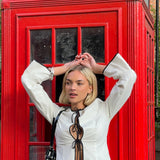 Fitted top in white with long loose sleeves. EmiliaMD shirt is closed with three black tie bands in front and has a ruffle detail at the sleeve. The model is 175 cm and wears a size S/36.