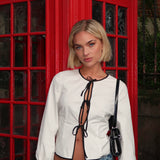Fitted top in white with long loose sleeves. EmiliaMD shirt is closed with three black tie bands in front and has a ruffle detail at the sleeve. The model is 175 cm and wears a size S/36.