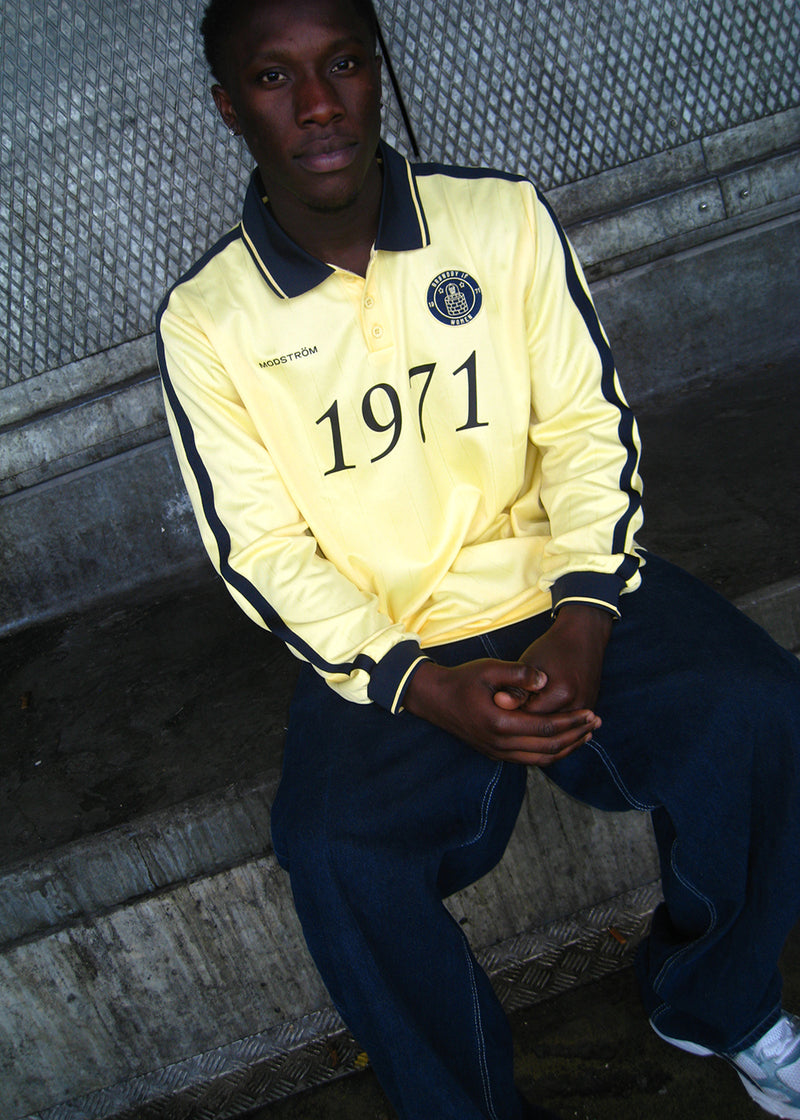 Football polo in yellow with navy blue details made in collaboration with Brøndby IF's women's team. The 1971 Polo has a loose fit with a placket closure and collar, as well as long sleeves with ribbed cuffs. The polo features the Brøndby IF Women and Modström logos on the chest.