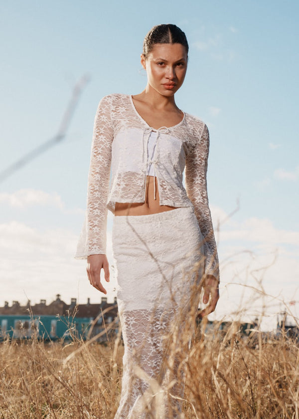 Fitted top in white stretchy lace with flared sleeves. TildeMD lace top has a deep V-neckline and two tiebands in the front.