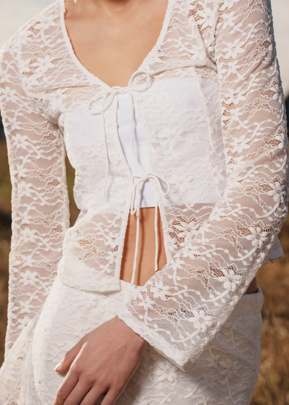 Fitted top in white stretchy lace with flared sleeves. TildeMD lace top has a deep V-neckline and two tiebands in the front.