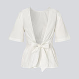 Feminine top with an open back and tie detail. The AikaMD Top features short sleeves, a round neckline, an A-line hem with pleating, and an attached band that cinches at the waist and ties at the back. The top is made from 100% organic cotton.