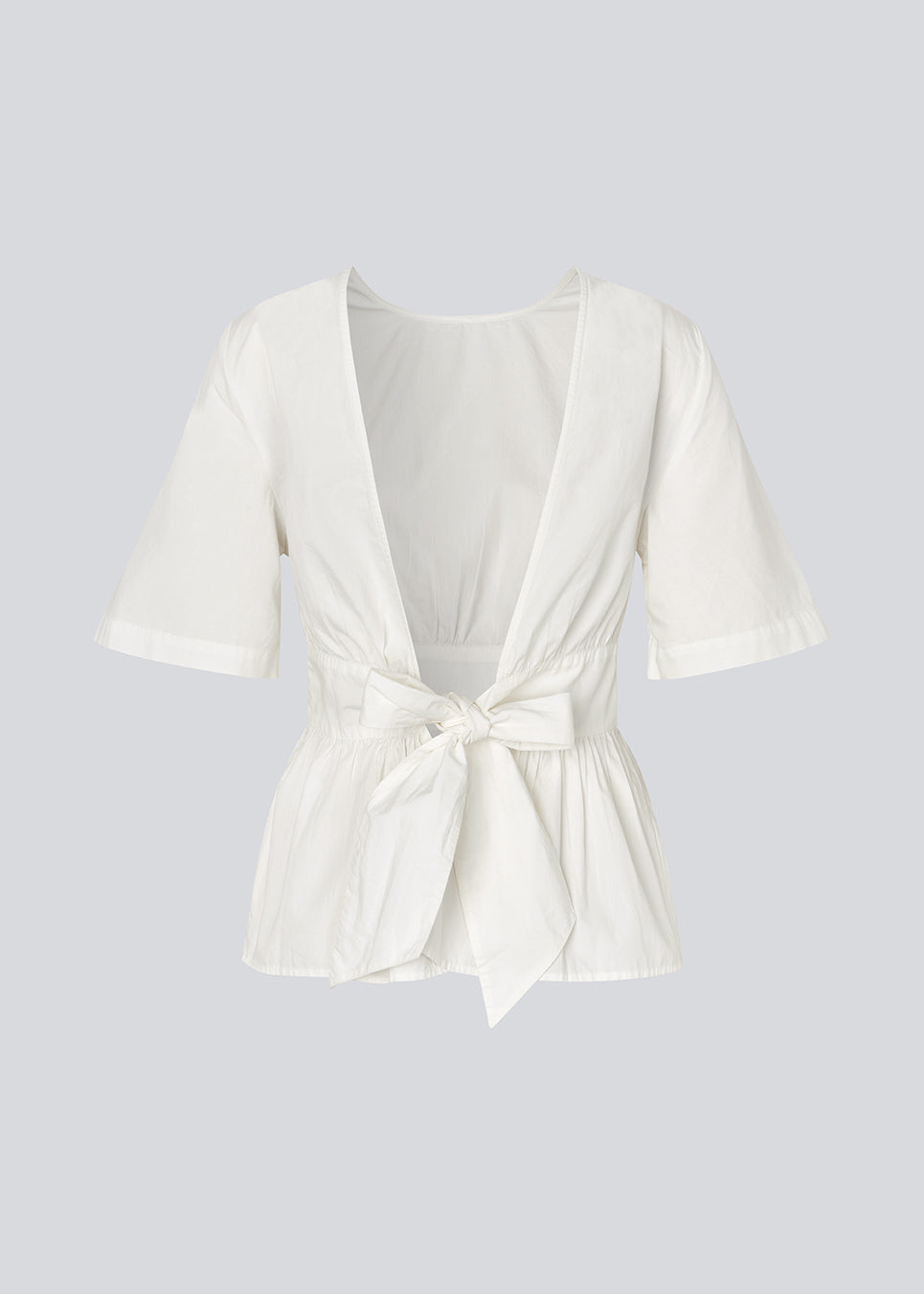 Feminine top with an open back and tie detail. The AikaMD Top features short sleeves, a round neckline, an A-line hem with pleating, and an attached band that cinches at the waist and ties at the back. The top is made from 100% organic cotton.