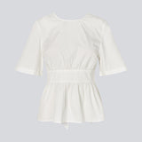 Feminine top with an open back and tie detail. The AikaMD Top features short sleeves, a round neckline, an A-line hem with pleating, and an attached band that cinches at the waist and ties at the back. The top is made from 100% organic cotton.
