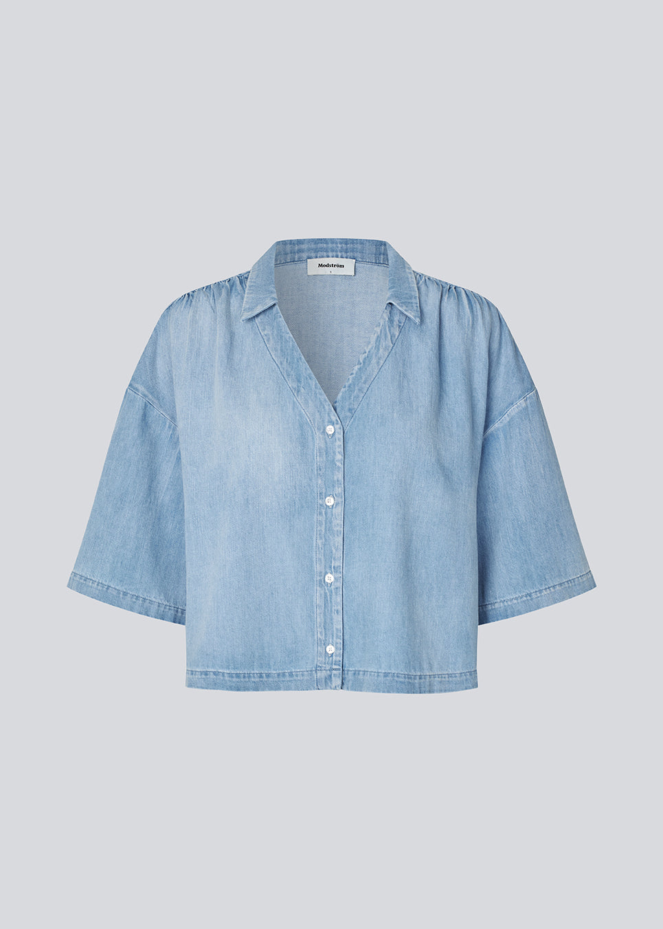 Light short-sleeve shirt in cotton denim. The AlvarMD Shirt is short and relaxed with a collar, V-neckline, and button closure. A casual and modern shirt, perfect for both everyday wear and light summer looks.