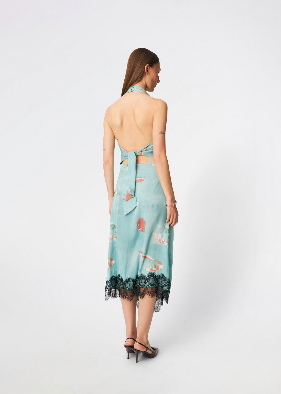Elegant maxi dress featuring an artistic print and feminine details. Carinamd print dress is crafted from a lightweight, smooth fabric with a high halterneck neckline that fastens at the back of the neck and a self-tie belt at the waist to define the silhouette. The long, flowing fit is finished with a contrasting lace trim at the hem, adding a refined and romantic touch. A standout dress, perfect for summer parties, weddings, and other special occasions.