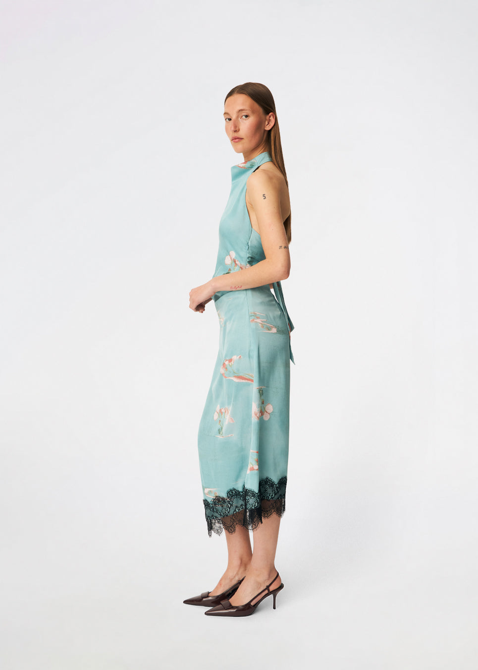 Elegant maxi dress featuring an artistic print and feminine details. Carinamd print dress is crafted from a lightweight, smooth fabric with a high halterneck neckline that fastens at the back of the neck and a self-tie belt at the waist to define the silhouette. The long, flowing fit is finished with a contrasting lace trim at the hem, adding a refined and romantic touch. A standout dress, perfect for summer parties, weddings, and other special occasions.
