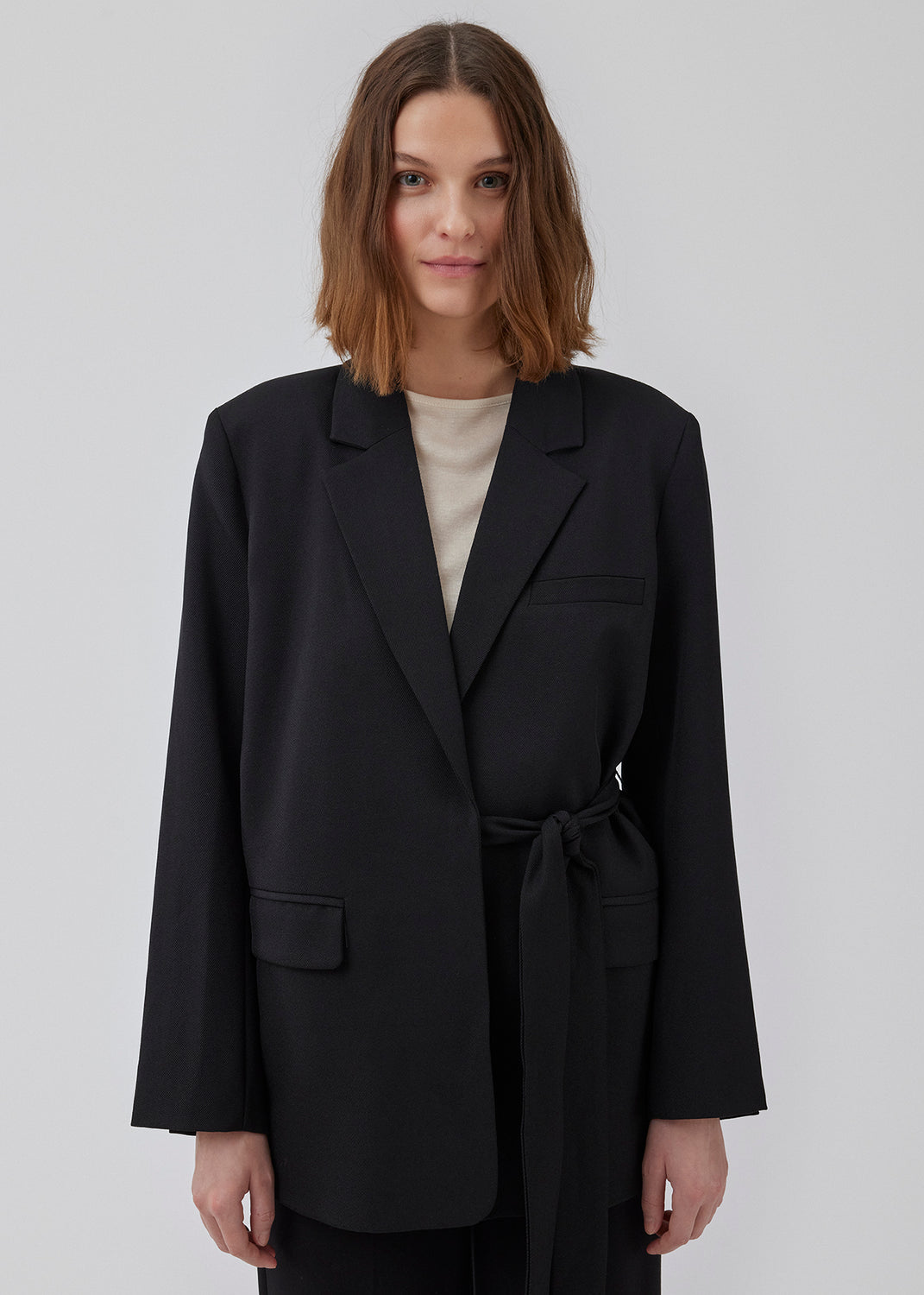 CayaMD blazer in black is designed for a relaxed fit with classic details with a twist from the tie-belt at the waist. Made from recycled materials. 