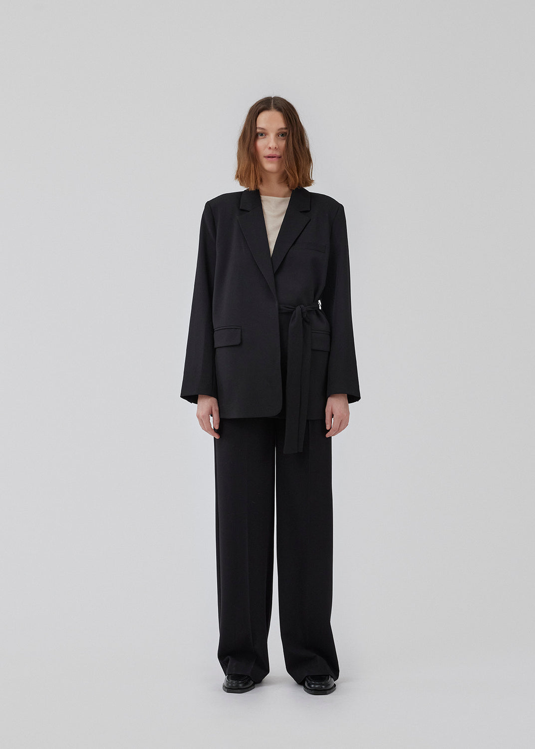 CayaMD blazer in black is designed for a relaxed fit with classic details with a twist from the tie-belt at the waist. Made from recycled materials. 