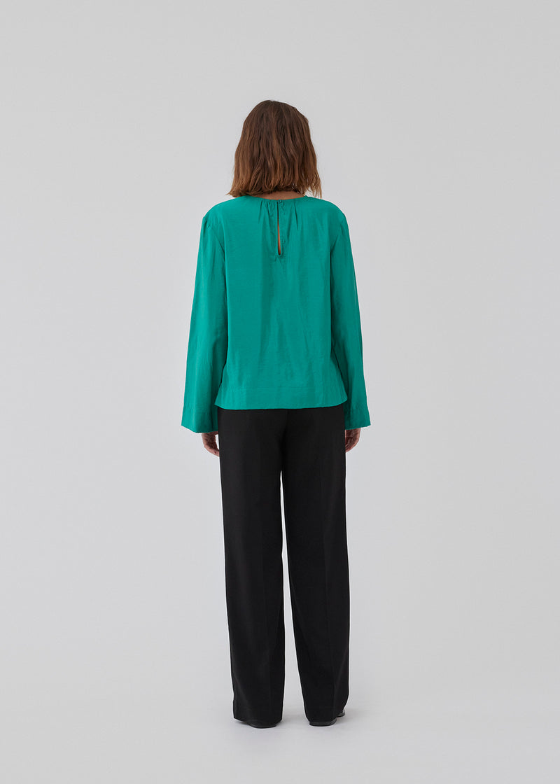 ChristopherMD top in green has a regular body with a round neck with gatherings, and small opening with button closure in the back. Long, wide sleeves. The model is 175 cm and wears a size S/36.