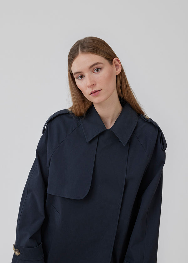 Short trench coat in dar blue in a cotton quality with concealed buttons down the front. Clara jacket has an oversized silhouette and classic details. Lined.