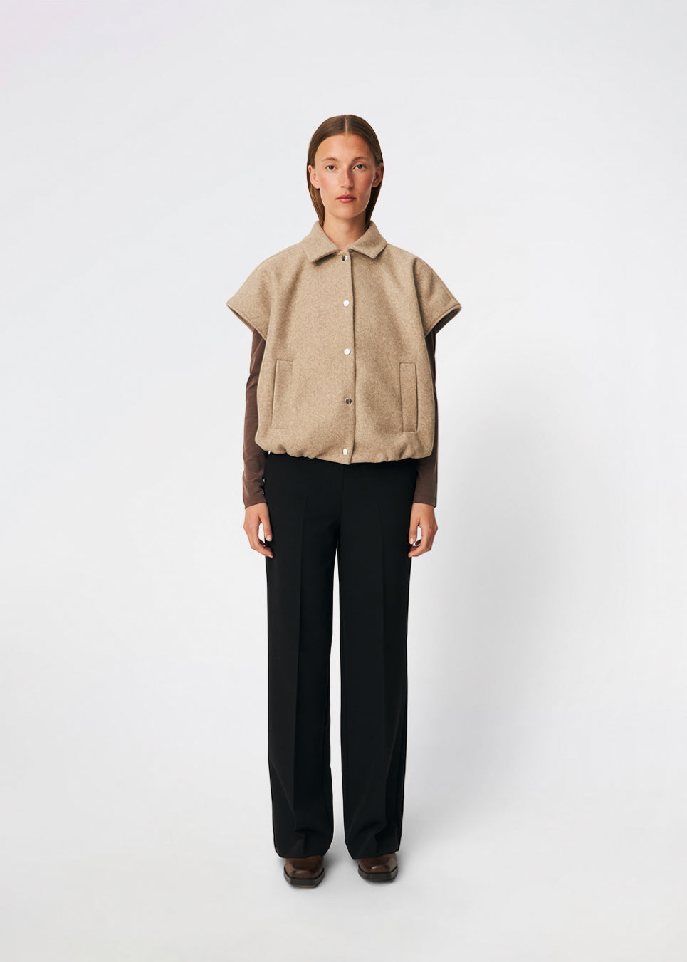 Short vest with a modern, relaxed aesthetic. Cleamd vest features a boxy silhouette with short, wide sleeves, a classic collar, and snap button closure at the front. Discreet front pockets and an elasticated hem create a soft, rounded shape and a comfortable fit. Perfect for layering over knitwear, shirts, or dresses during the transitional seasons.
