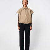 Short vest with a modern, relaxed aesthetic. Cleamd vest features a boxy silhouette with short, wide sleeves, a classic collar, and snap button closure at the front. Discreet front pockets and an elasticated hem create a soft, rounded shape and a comfortable fit. Perfect for layering over knitwear, shirts, or dresses during the transitional seasons.
