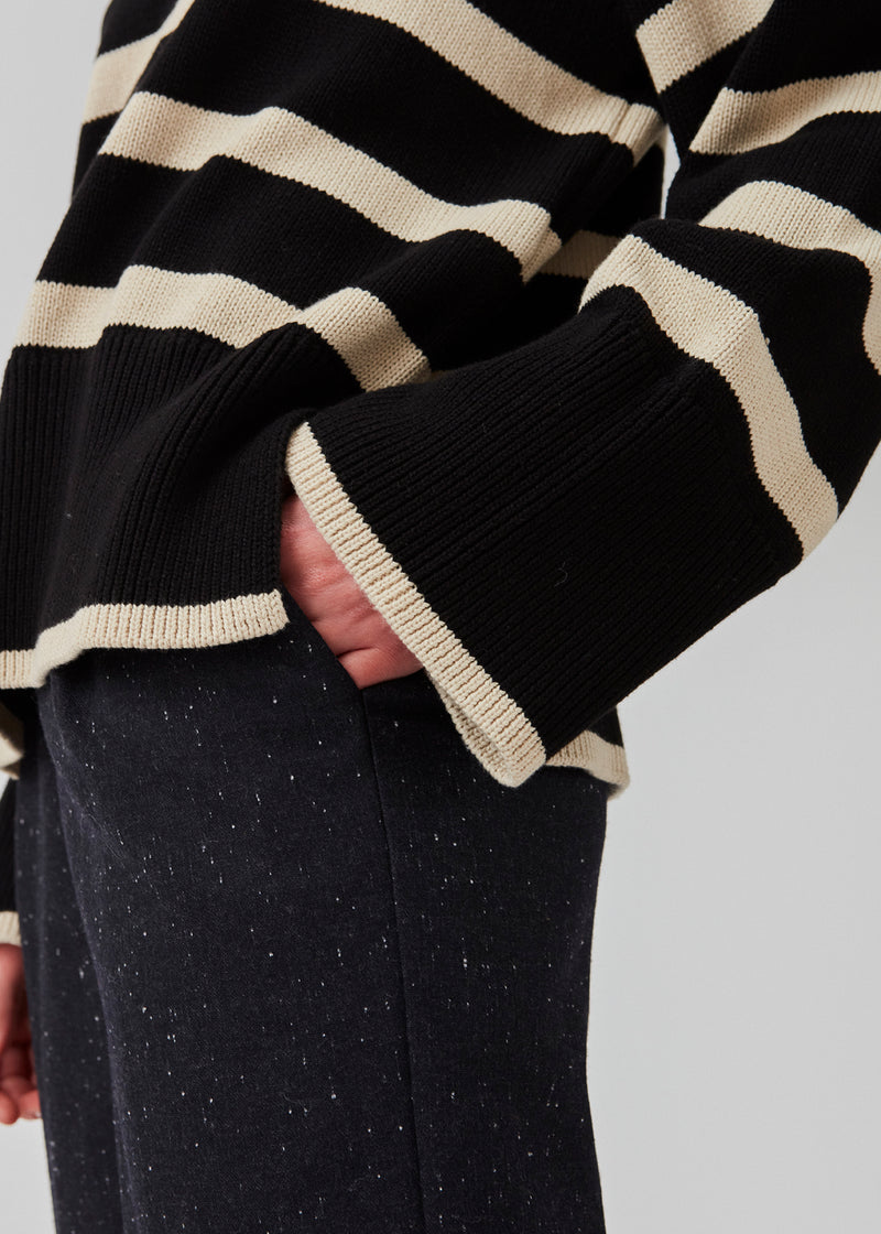 Fine-knitted oversized jumper knitted from cotton in black with beige stripes. CorbinMD stripe t-neck has a ribbed rollneck, long wide sleeves, and wide ribbing at cuffs and hem.  The model is 177 cm and wears a size S/36.