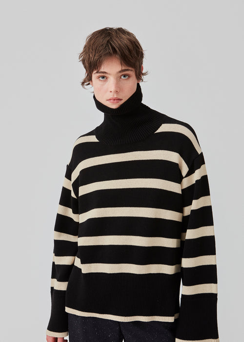 Fine-knitted oversized jumper knitted from cotton in black with beige stripes. CorbinMD stripe t-neck has a ribbed rollneck, long wide sleeves, and wide ribbing at cuffs and hem.  The model is 177 cm and wears a size S/36.