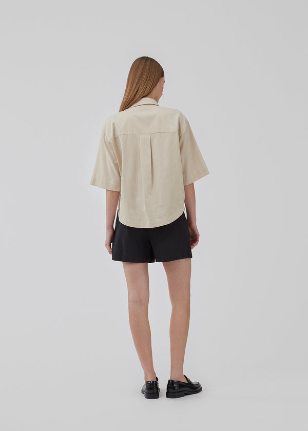 Short, oversized shirt in cotton in beige. CydneyMD ss shirt has a collar, button closure in front, and rounded hems at the bottom. Dropped shoulders and short sleeves. The model is 175 cm and wears a size S/36.