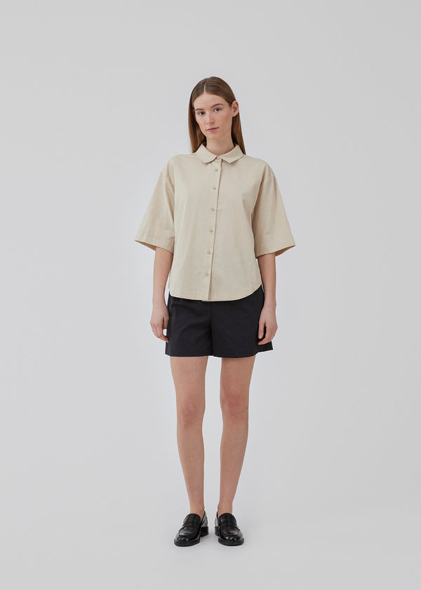 Short, oversized shirt in cotton in beige. CydneyMD ss shirt has a collar, button closure in front, and rounded hems at the bottom. Dropped shoulders and short sleeves. The model is 175 cm and wears a size S/36.
