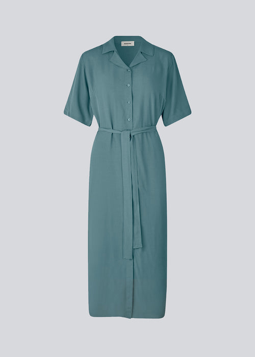 Relaxed shirt dress in blue made from EcoVero viscose. DafneMD long dress has a resort collar, button closure in front, tie belt at the waist, and short sleeves. The model is 177 cm and wears a size S/36.