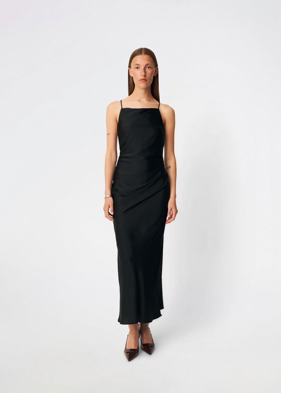 DanillaMD Dress is a long satin dress with an elegant, figure-hugging silhouette. The design features a straight neckline, thin straps and draped detailing at the side, creating a soft fall. The open back with delicate crossing straps adds a feminine touch. Style it with heels and simple accessories for special occasions. The model is 175 cm tall and is wearing a size S/36.