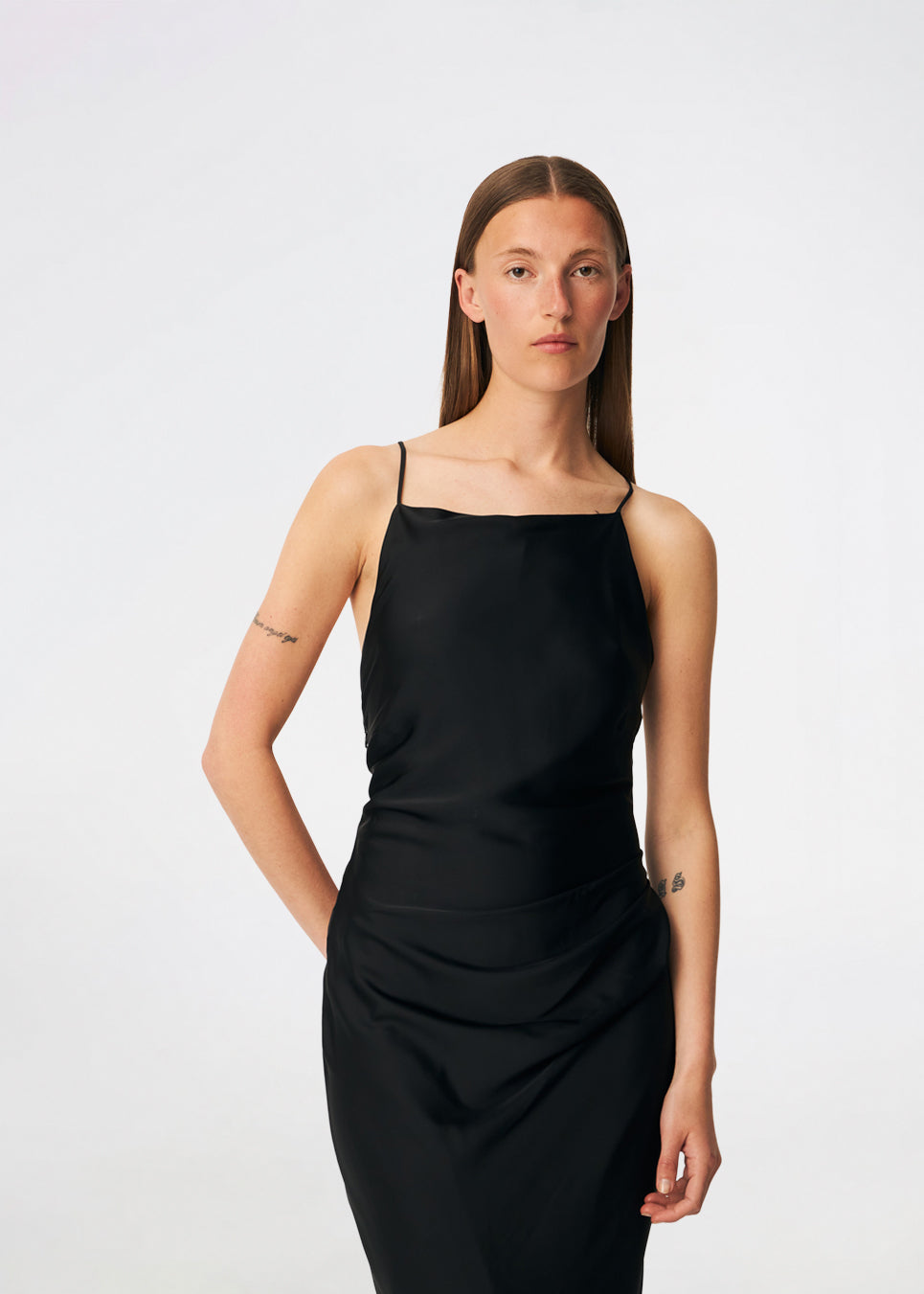 DanillaMD Dress is a long satin dress with an elegant, figure-hugging silhouette. The design features a straight neckline, thin straps and draped detailing at the side, creating a soft fall. The open back with delicate crossing straps adds a feminine touch. Style it with heels and simple accessories for special occasions. The model is 175 cm tall and is wearing a size S/36.