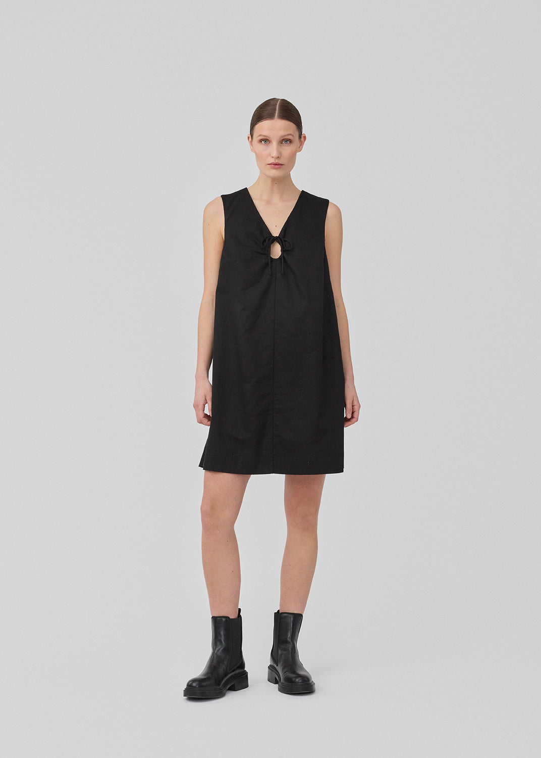 Short black linen dress with an A-line silhouette. DaynaMD dress is sleeveless, and features a deep v-neckline with cut-out details and ties. The model is 177 cm and wears a size S/36.