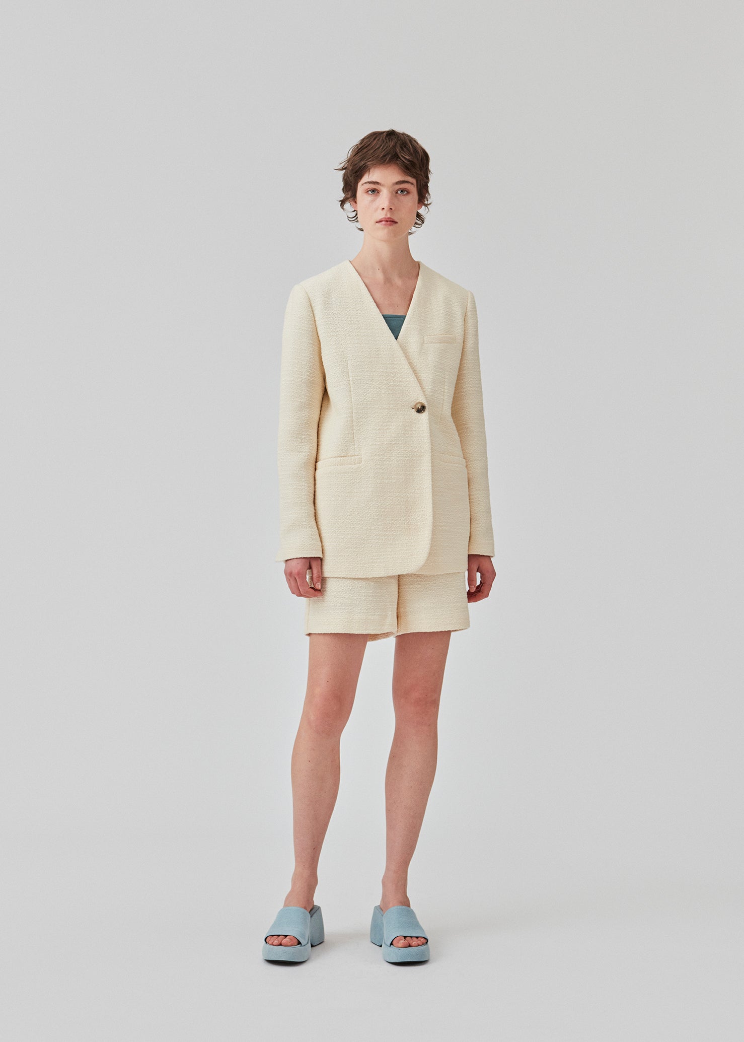 DimeMD blazer is designed in a textured cotton blend with lining. The blazer is collarless but has an asymmetrical wrap detail with a single visible button. The model is 177 cm and wears a size S/36.  Style the blazer with matching shorts: DimeMD shorts.