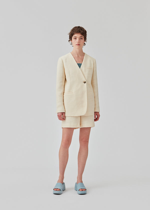 DimeMD blazer is designed in a textured cotton blend with lining. The blazer is collarless but has an asymmetrical wrap detail with a single visible button. The model is 177 cm and wears a size S/36.  Style the blazer with matching shorts: DimeMD shorts.
