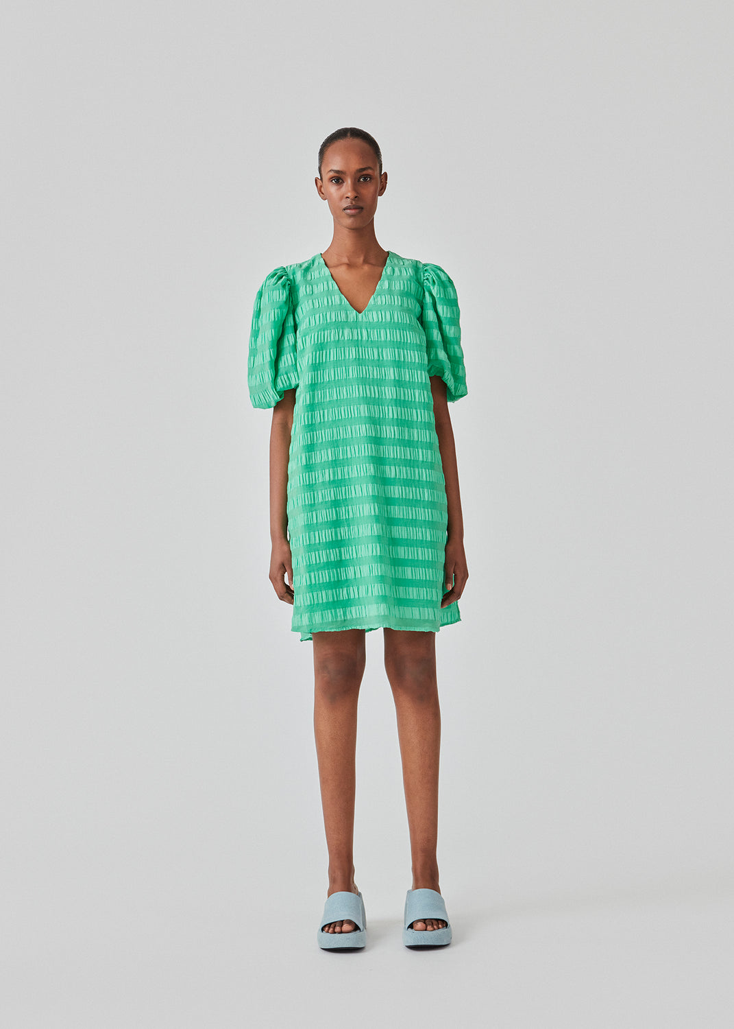 Short dress in green in a seersucker material. DinoMD dress has a v-shaped neckline, a loose silhouette, and short puff sleeves with elastic. The model is 177 cm and wears a size S/36.