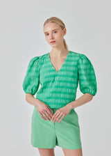 DinoMD top in green is designed in a seersucker material with a relaxed fit. The top has a v-neckline and short puff sleeves with elasticated cuffs. The model is 177 cm and wears a size S/36.