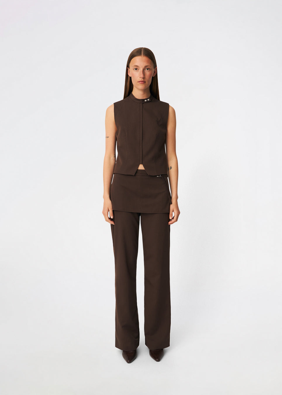The Dodomd Pants feature a straight-leg silhouette with an integrated skirt overlay that creates a modern, statement look. A slim waist strap with a metal buckle adds a refined finishing touch, while the clean tailoring makes them easy to style. Pair them with the matching Dodomd Top or a simple knit for an elevated everyday outfit.