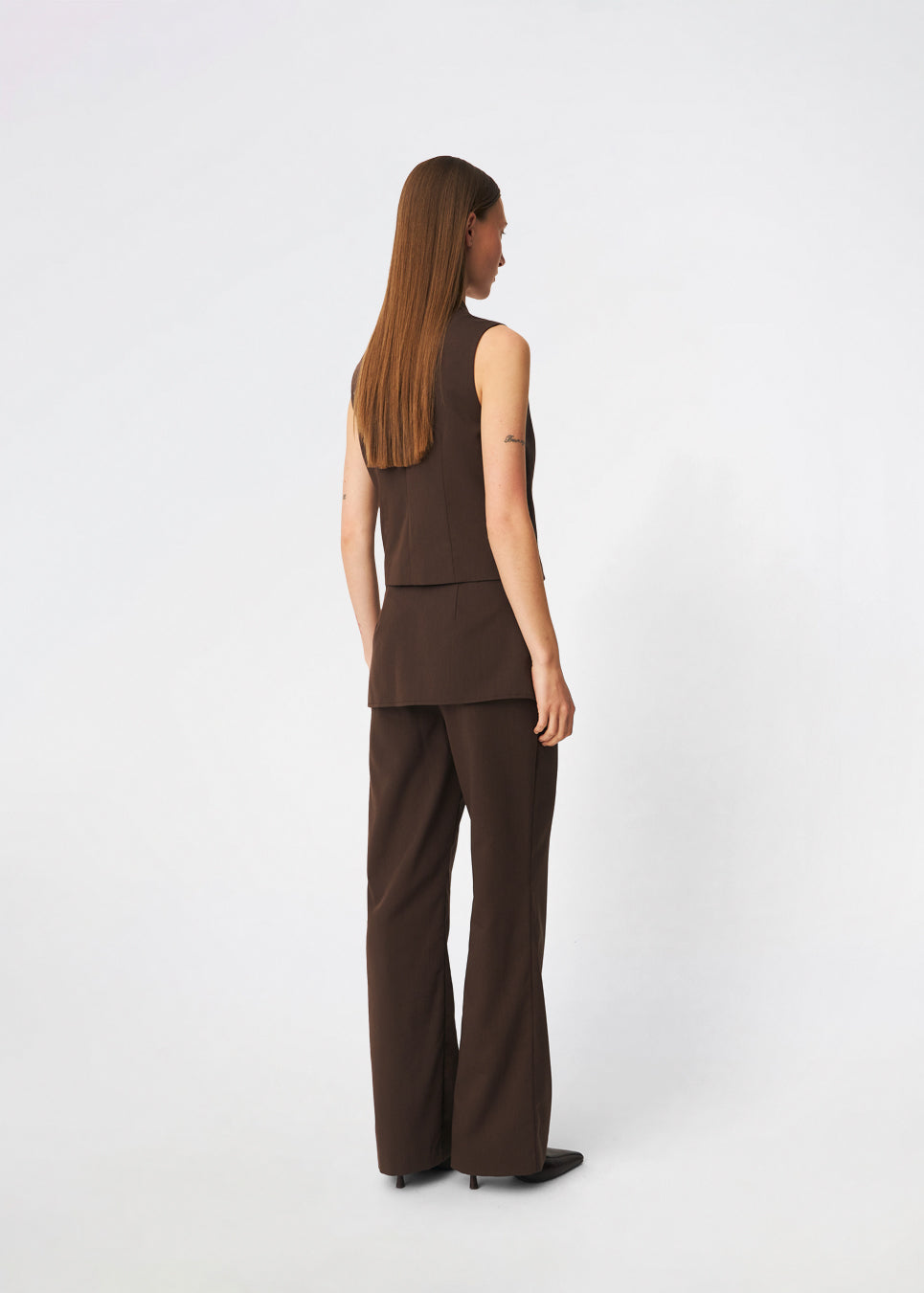 The Dodomd Top is an elegant sleeveless top with a clean, tailored silhouette. The high neckline with decorative press buttons and concealed front closure create a modern, minimalist look, while the shaping seams enhance the fit. Wear it on its own or style it with the matching trousers for a refined coordinated outfit.