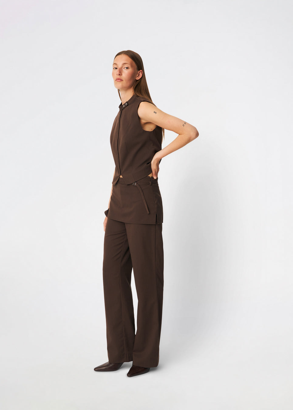 The Dodomd Top is an elegant sleeveless top with a clean, tailored silhouette. The high neckline with decorative press buttons and concealed front closure create a modern, minimalist look, while the shaping seams enhance the fit. Wear it on its own or style it with the matching trousers for a refined coordinated outfit.