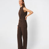 The Dodomd Top is an elegant sleeveless top with a clean, tailored silhouette. The high neckline with decorative press buttons and concealed front closure create a modern, minimalist look, while the shaping seams enhance the fit. Wear it on its own or style it with the matching trousers for a refined coordinated outfit.