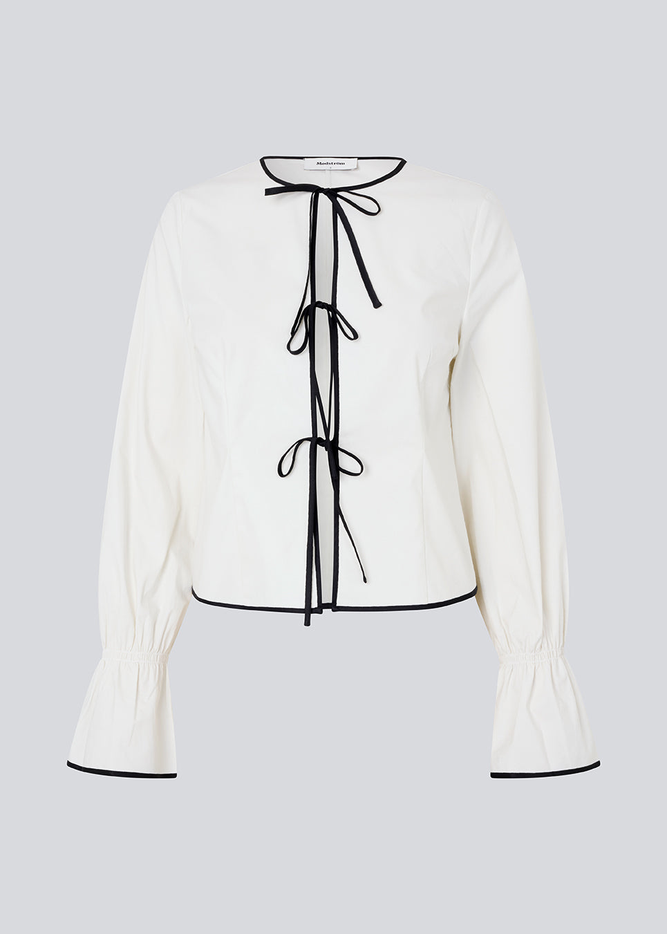 Fitted top in white with long loose sleeves. EmiliaMD shirt is closed with tree black tie bands in front and has a ruffle detail at the sleeve.