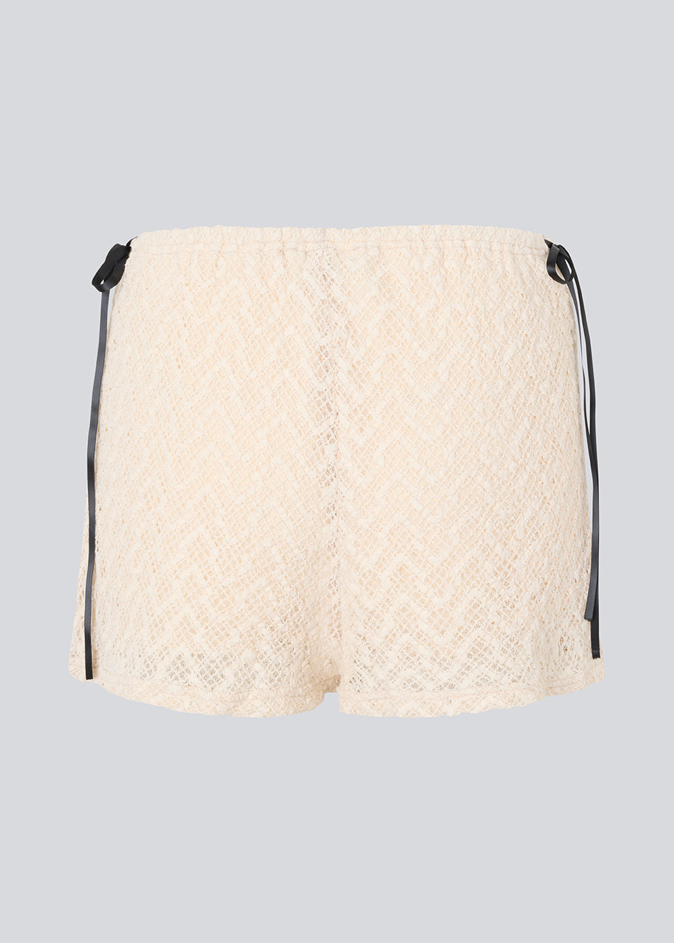 Cute shorts in a soft lace material in light beige/white. EmiliaMD lace shorts have lining and elastic at the waist. The shorts have two black bows on hips as a cool contrast to the light beige.