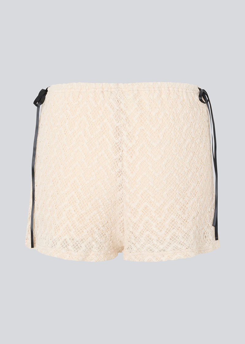 Cute shorts in a soft lace material in light beige/white. EmiliaMD lace shorts have lining and elastic at the waist. The shorts have two black bows on hips as a cool contrast to the light beige.