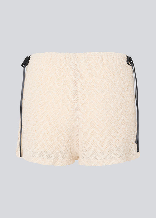 Cute shorts in a soft lace material in light beige/white. EmiliaMD lace shorts have lining and elastic at the waist. The shorts have two black bows on hips as a cool contrast to the light beige.