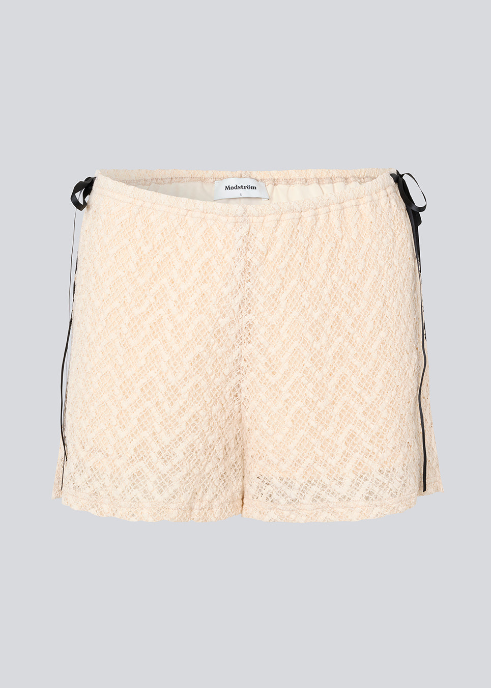 Cute shorts in a soft lace material in light beige/white. EmiliaMD lace shorts have lining and elastic at the waist. The shorts have two black bows on hips as a cool contrast to the light beige.
