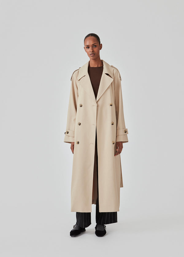 Oversized double-breasted trench coat in light beige with tie belt at the waist. EvieMD jacket has dropped shoulders and long, wide sleeves. Lined. The model is 175 cm and wears a size S/36.