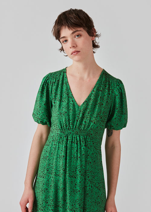 Maxi dress with a v-neckline with smock detail below the breast, on the shoulder and back. FalkeMD print dress has short puff sleeves and a loose skirt. The model is 175 cm and wears a size S/36.