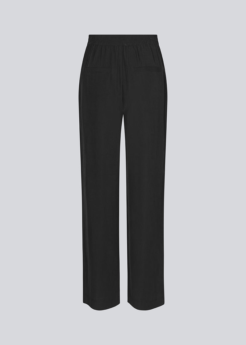 FanyaMD pants in black have a menswear-inspired look with straight, wide legs, a high waist with zip fly and button and elastication in back. Doubble pleat in front and side pockets. 