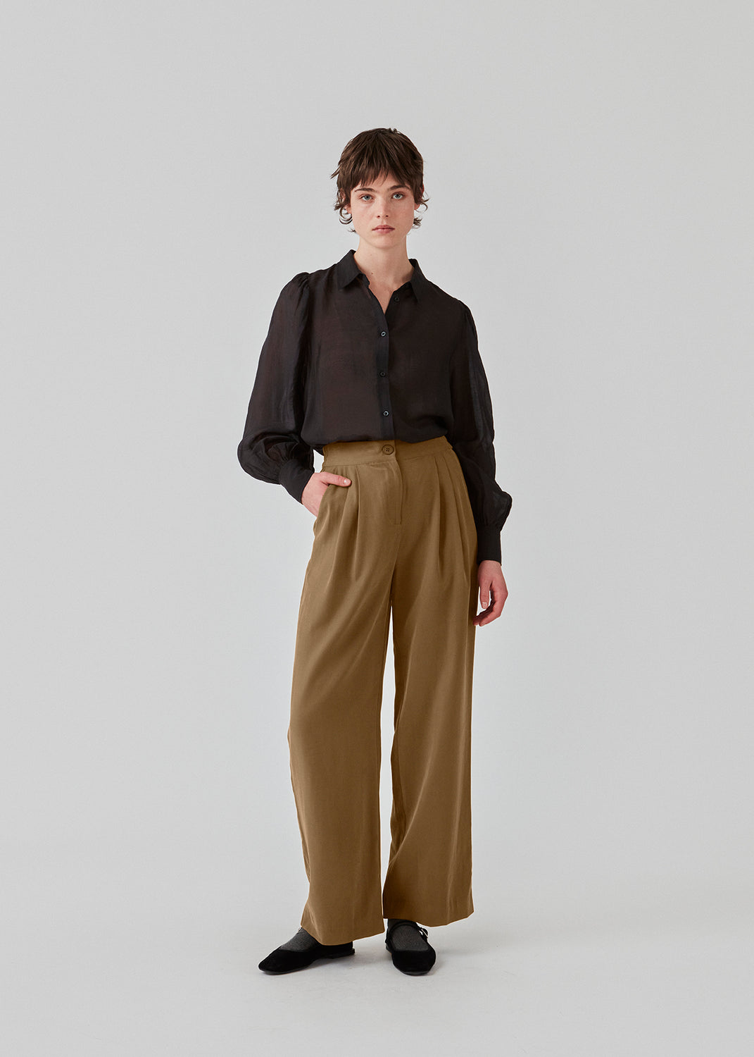 FanyaMD pants in brown have a menswear-inspired look with straight, wide legs, a high waist with zip fly and button and elastication in the back. Double pleat in front and side pockets. The model is 175 cm and wears a size S/36.