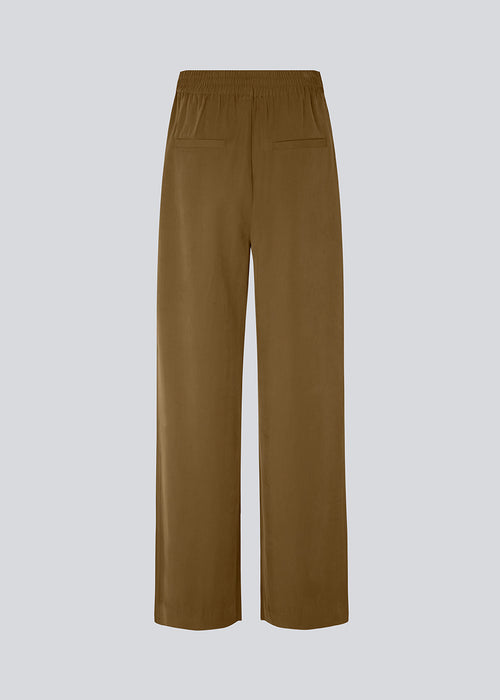 FanyaMD pants in brown have a menswear-inspired look with straight, wide legs, a high waist with zip fly and button and elastication in the back. Double pleat in front and side pockets. The model is 175 cm and wears a size S/36.