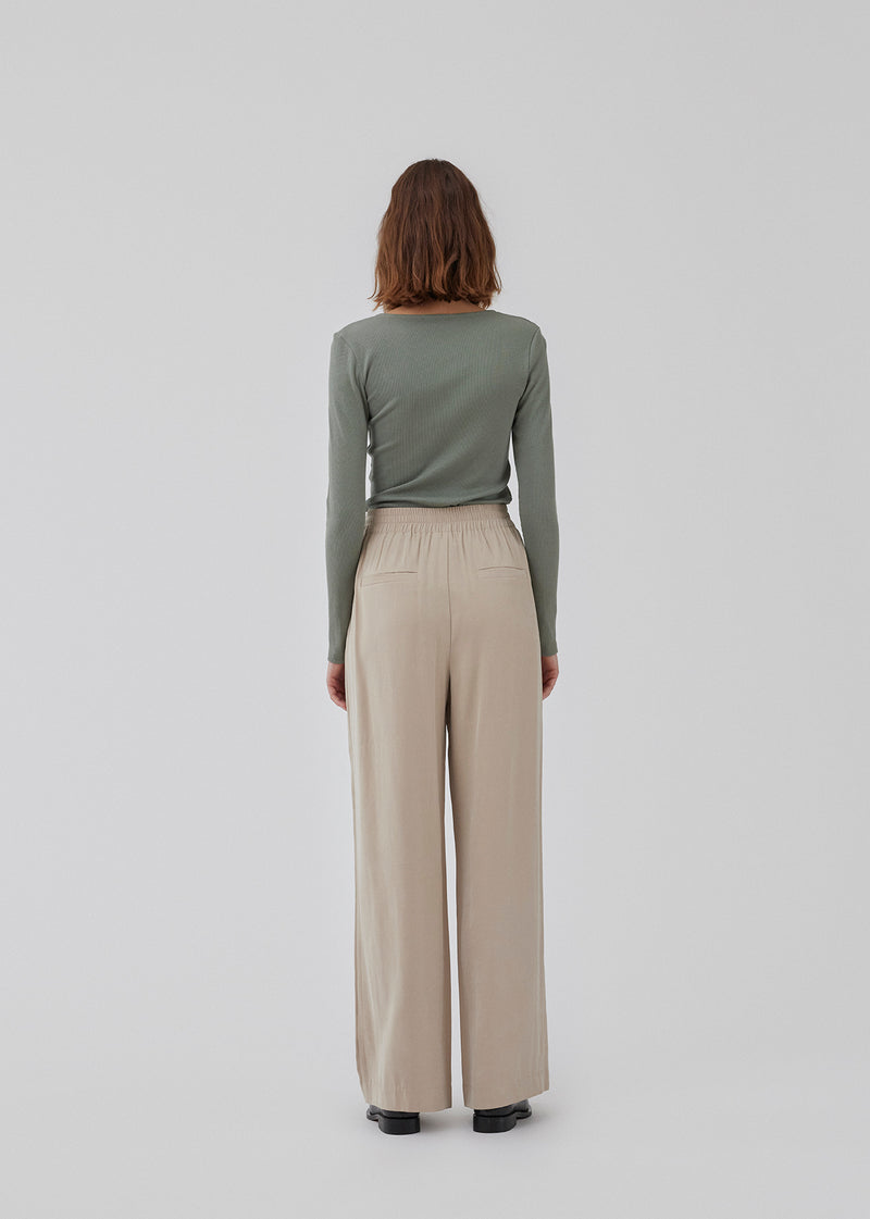 FanyaMD pants in bright beige have a menswear-inspired look with straight, wide legs, a high waist with zip fly and button and elastication in back. Doubble pleat in front and side pockets. The model is 175 cm and wears a size S/36.